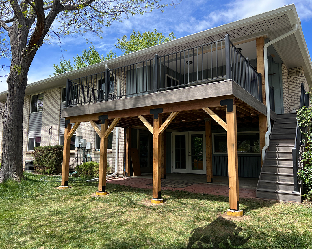 Two-story wooden deck with black railings on a brick house.