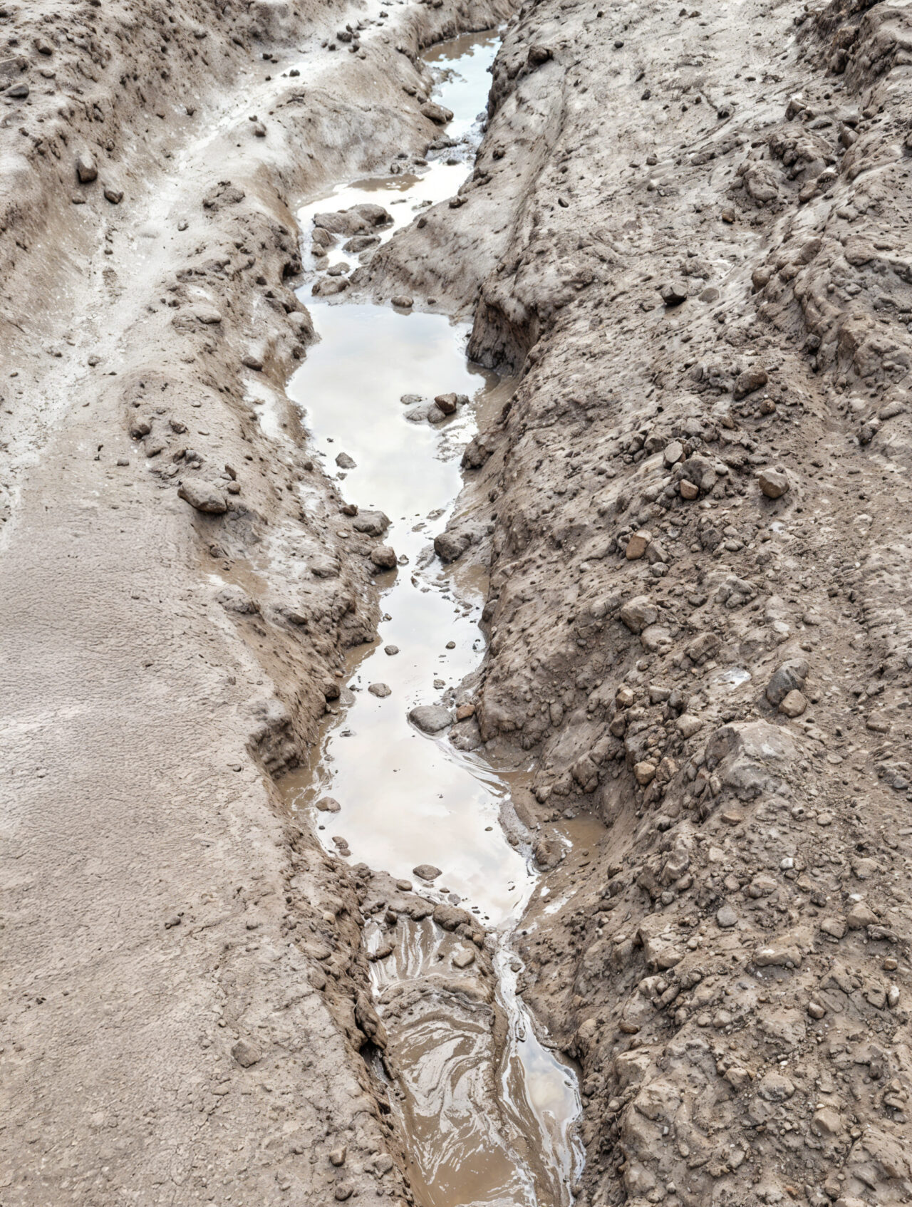 White house by a stream with a view of a forested hill.